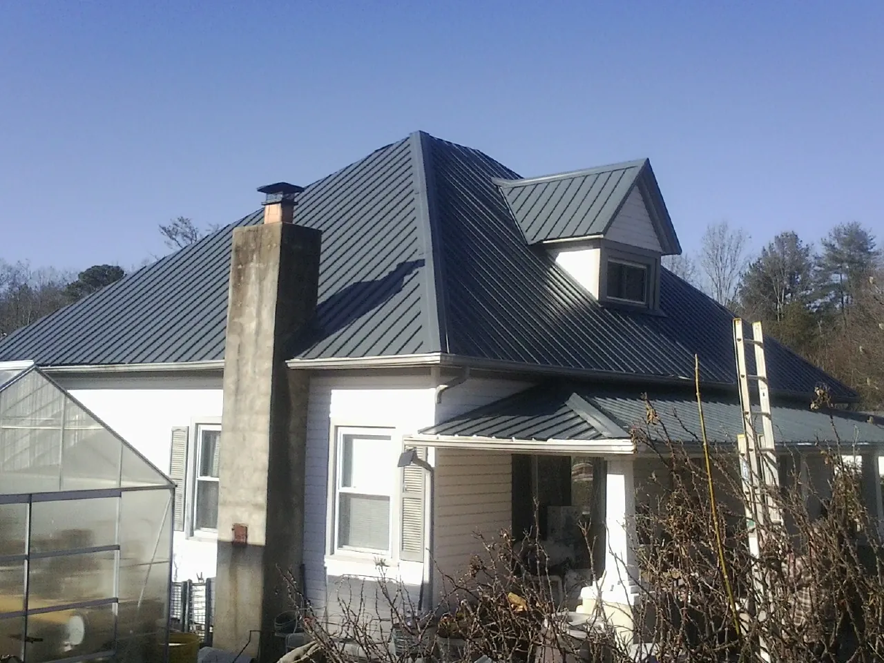 Dark blue standing seam metal roof on a white farmhouse with dormer — Slate & Tile Roof Repair by Roofing Brothers in Eglon