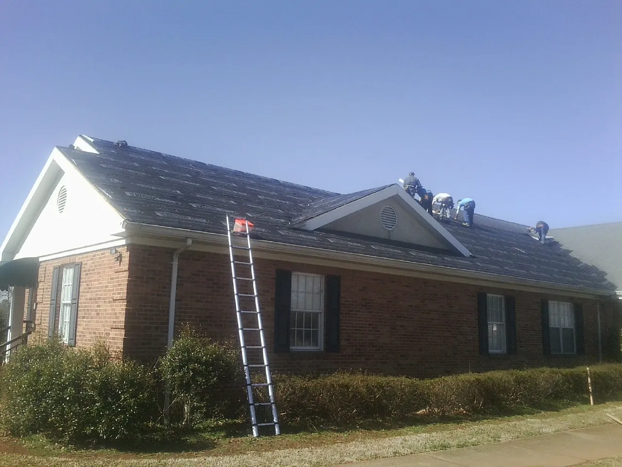Crew tearing shingles off a brick ranch roof with a ladder set — Metal Roof Repair work by our crew in Eglon
