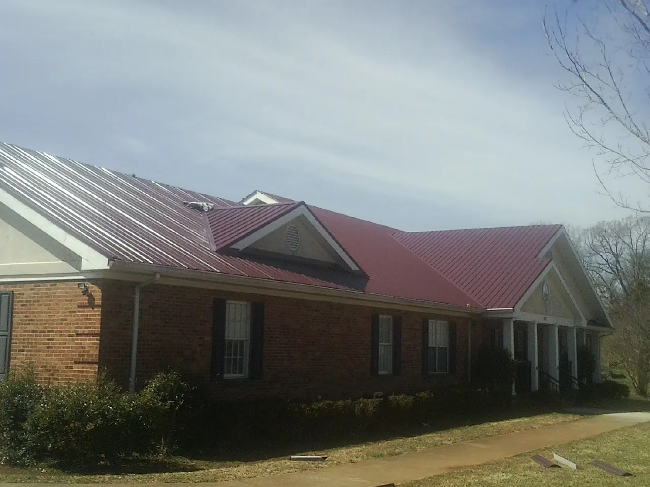 Red metal roof with gabled entries on a long brick building, from a Hail Damage Roof Repair job in Eglon