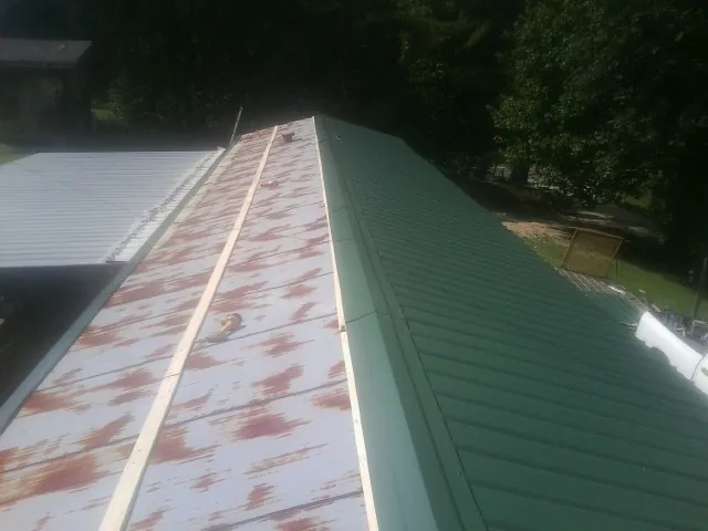 Old rusted panels beside newly installed green metal roofing — Wind Damage Roof Repair by Roofing Brothers in Eglon