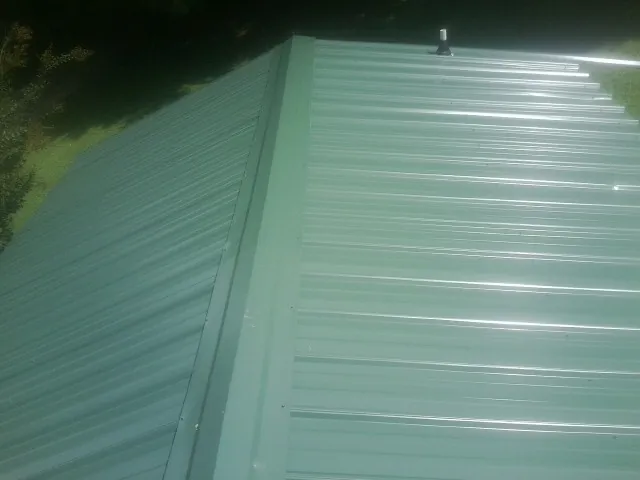New green metal panels meeting at the ridge of a roof — Flat Roof Repair work by our crew in Eglon