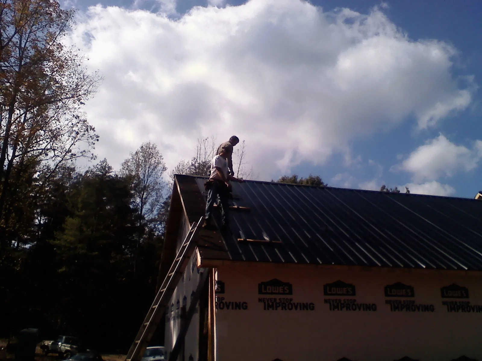 Roofer fastening dark metal panels high against a cloudy sky, from a Roof Inspection job in Eglon